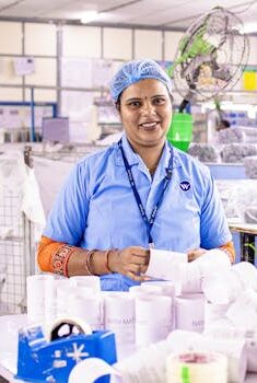 Confident female factory worker inspects and organizes textile products at a bustling industrial facility.